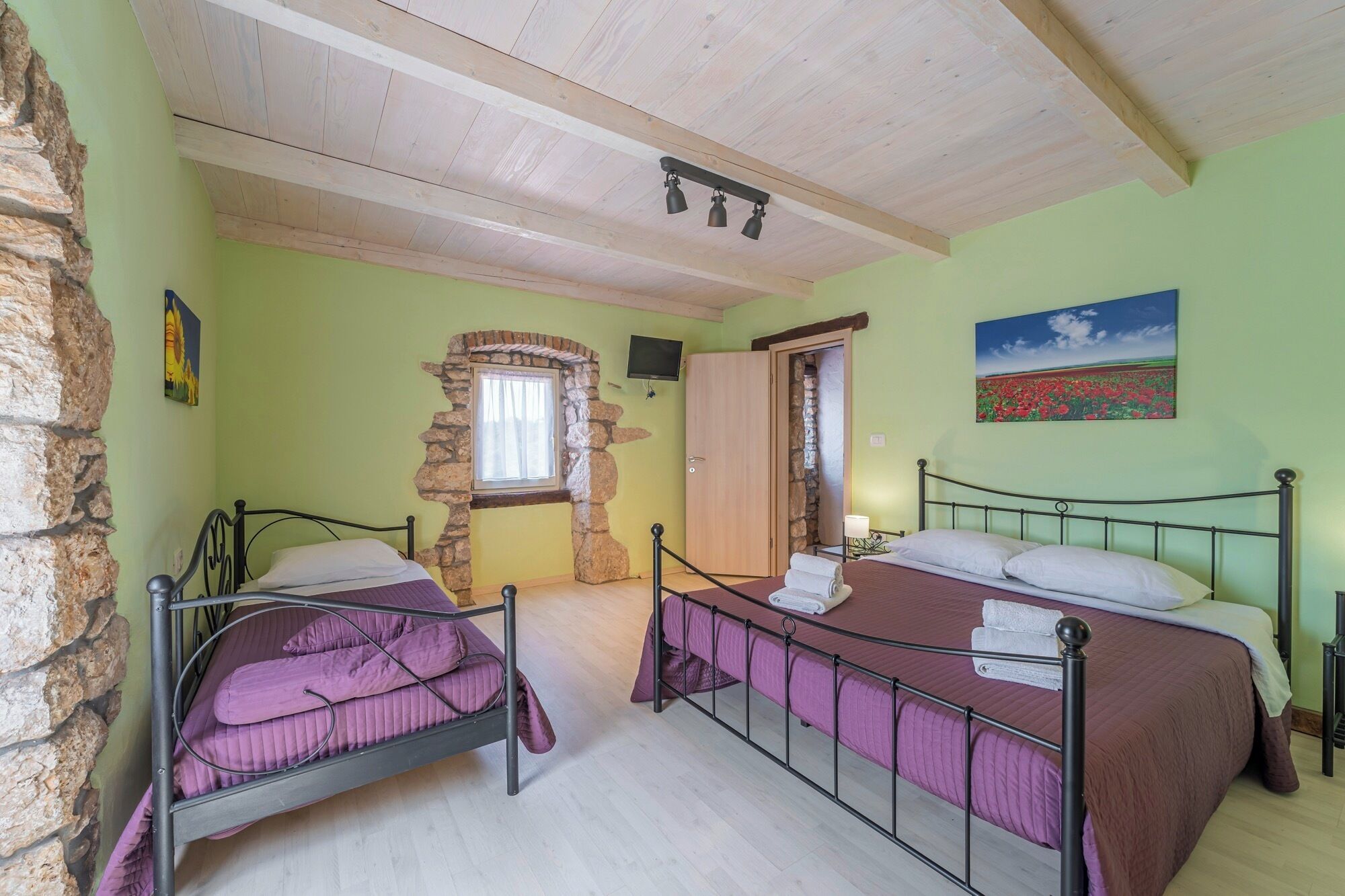 A room with two beds, a stone wall, a wooden ceiling, and a painting on the wall.
