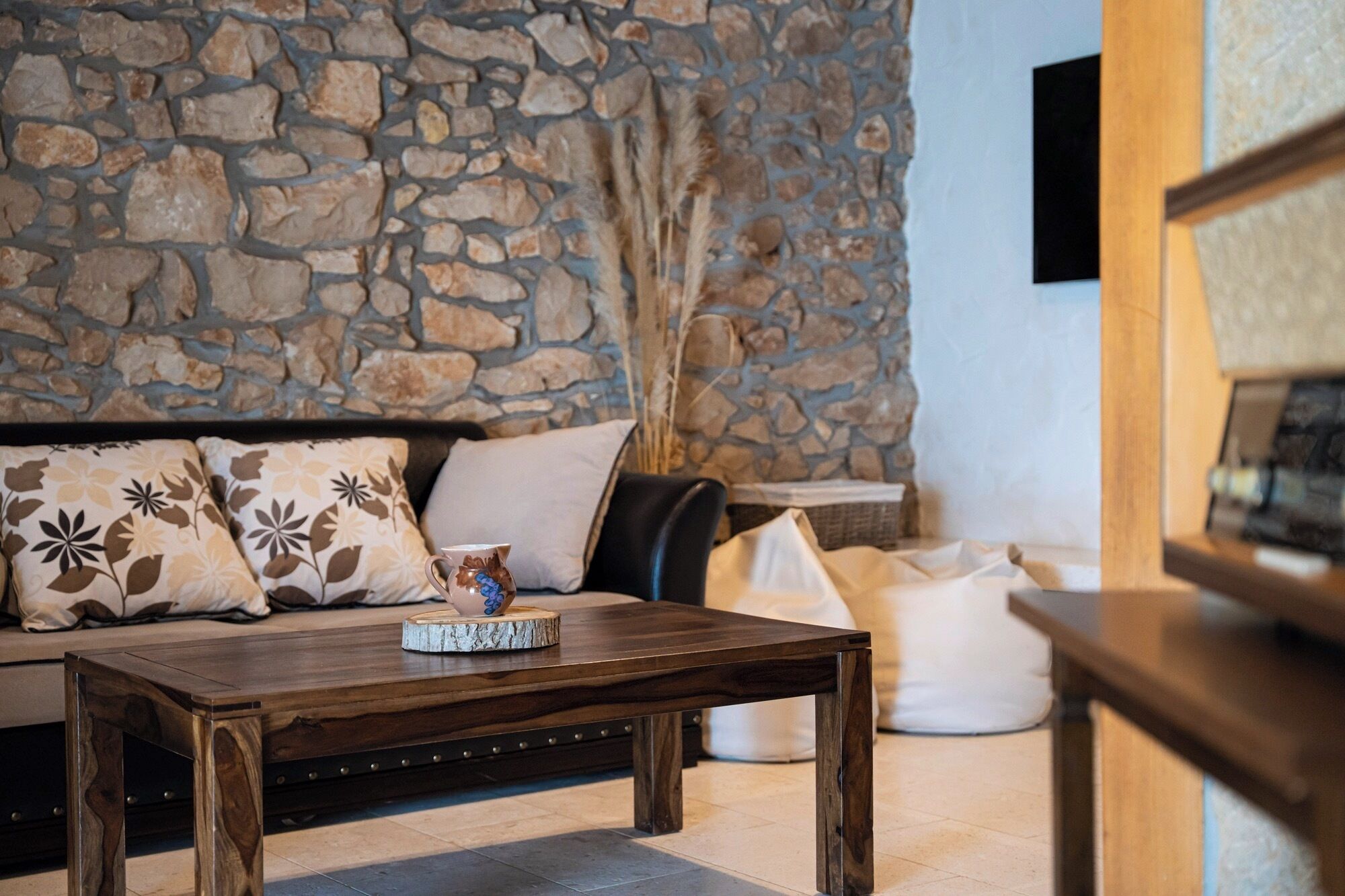 Un salón acogedor con una pared de piedra, un sofá con cojines estampados, una mesa de centro de madera y un banquito blanco.