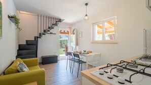 Een moderne keuken met een gasfornuis, een eethoek met een tafel en stoelen, een trap met een zwarte balustrade, en uitzicht op de omgeving via een raam.