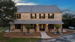 A two-story stone building with a metal roof, multiple windows, and a front porch with benches. - The Point-Hill Country Views-Pool+Hot Tub (Fredericksburg)