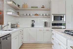 A modern kitchen with white cabinetry, a built-in microwave, and a dishwasher. - The Point-Hill Country Views-Pool+Hot Tub (Fredericksburg)
