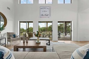 A spacious living room with a large coffee table, seating area, and a view of the outdoors through large sliding glass doors. - The Point-Hill Country Views-Pool+Hot Tub (Fredericksburg)