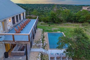 A poolside area with lounge chairs, a pool, and a building with a balcony. - The Point-Hill Country Views-Pool+Hot Tub (Fredericksburg)