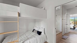 A bunk bed with white bedding and a wooden ladder, a small bedside table, and a door leading to a balcony. - The Point-Hill Country Views-Pool+Hot Tub (Fredericksburg)