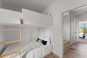 A bunk bed with white bedding and a wooden ladder, a small bedside table, and a door leading to a balcony. - The Point-Hill Country Views-Pool+Hot Tub (Fredericksburg)