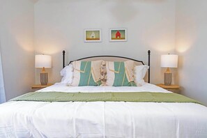 A neatly made bed with a green throw, two bedside lamps, and two framed pictures on the wall. - The Point-Hill Country Views-Pool+Hot Tub (Fredericksburg)