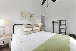 A neatly arranged bedroom with a bed, two bedside tables with lamps, a wall-mounted shelf, and framed floral artwork. - The Point-Hill Country Views-Pool+Hot Tub (Fredericksburg)