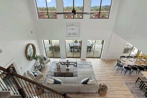 A spacious living area with a high ceiling, large windows, and a central seating area with a coffee table.