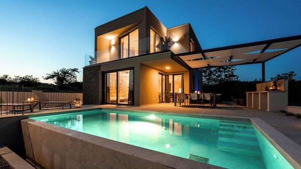 Et moderne hus med to etager, en swimmingpool, store vinduer og udendørs siddepladser.