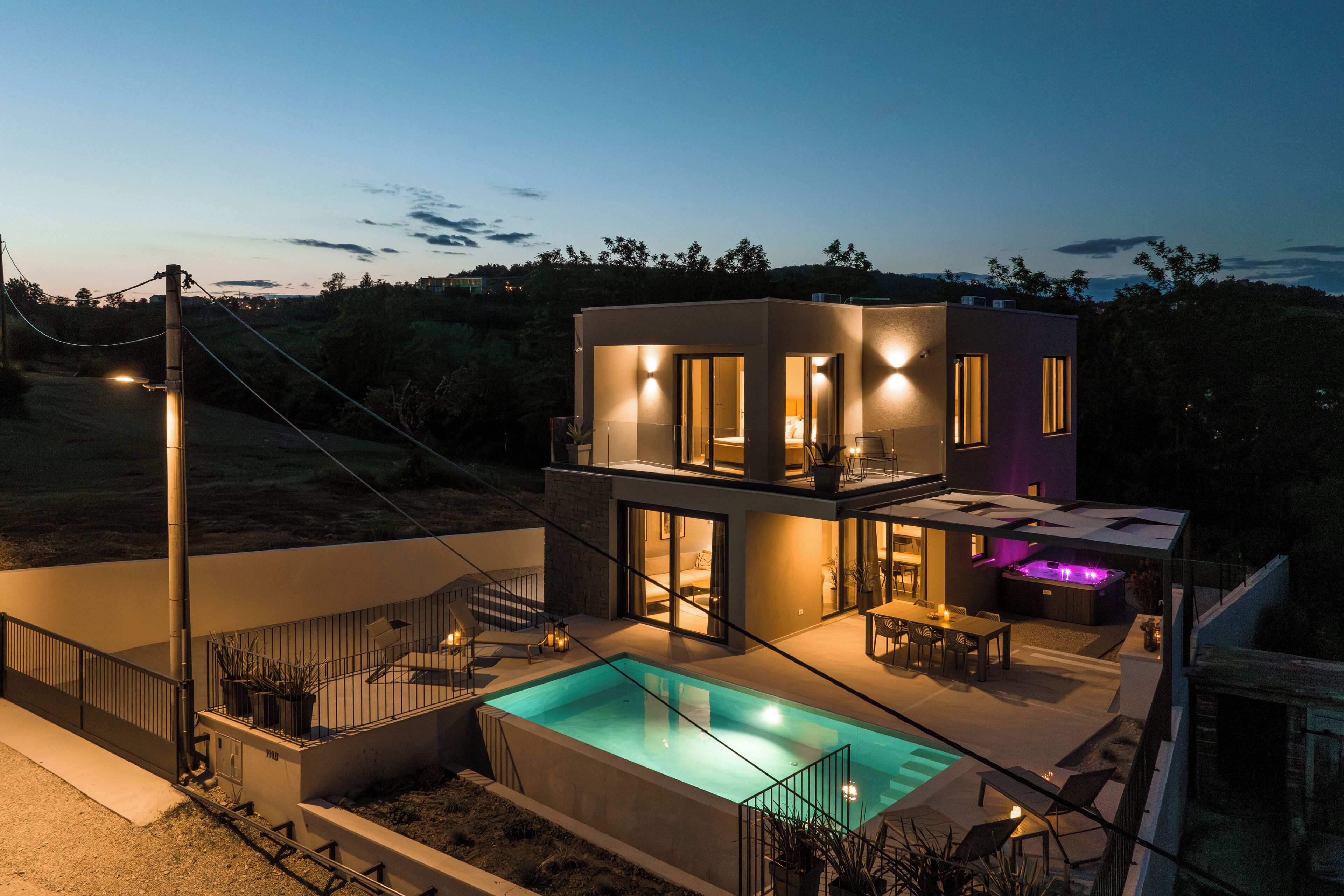A modern two-story house with a swimming pool, outdoor seating, and a well-lit patio area.