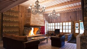Un intérieur chaleureux de chalet avec une cheminée en pierre, des fauteuils en cuir et un lustre.