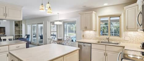 A modern kitchen with white cabinets, a central island, and a dining area with a table and chairs.