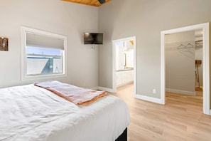 A bedroom with a bed, a TV, a window, and a view of a building outside.