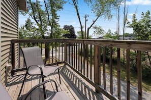 A wooden deck with two chairs and a grill, overlooking a street and trees.