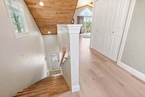 A staircase with wooden steps and a white handrail, leading to a room with a white door and a window with blinds.