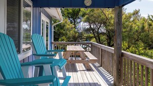 Una terraza de madera con sillas Adirondack y una mesa de picnic, con vistas a una zona boscosa.