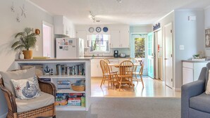 Una cocina moderna con armarios blancos, un comedor con sillas de madera y una estantería llena de libros de viajes.