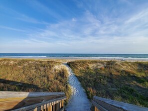 Un sentier bordé de dunes et de rambardes en bois, qui mène à l’océan.