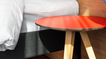 A modern room with a bed, a red table, and a wooden floor.