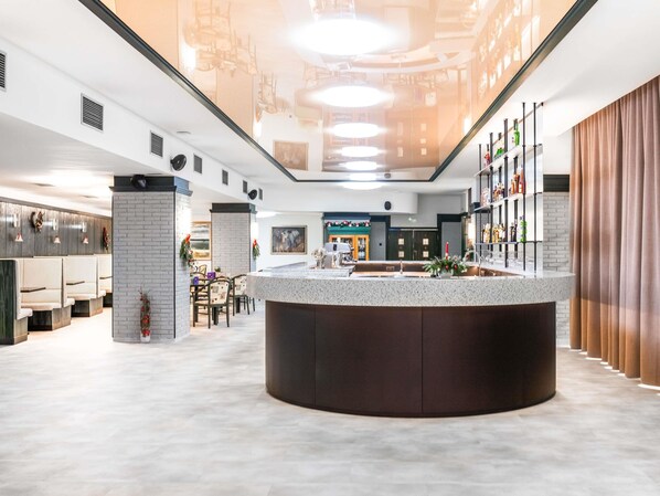 A modern hotel lobby with a central bar area, seating arrangements, and a reception desk.