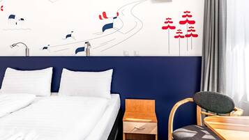 A hotel room with a bed, a desk, a chair, a small wooden cabinet, and a wall with abstract art.