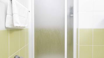 A bathroom with a white towel hanging on a rack, a glass shower door, and green tiled walls.