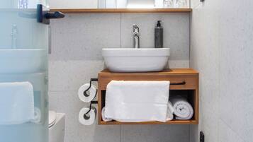 A modern bathroom with a white sink, wooden vanity, and a glass shower enclosure.