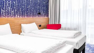 Habitación de hotel con dos camas, cabecera de madera, una silla roja y una ventana con cortinas traslúcidas.