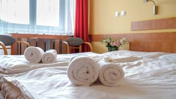 Cama bien hecha con toallas blancas enrolladas y un cabecero de madera.
