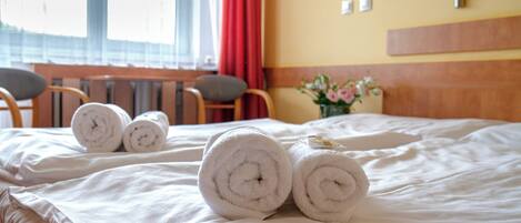 Cama bien hecha con toallas blancas enrolladas y un cabecero de madera.