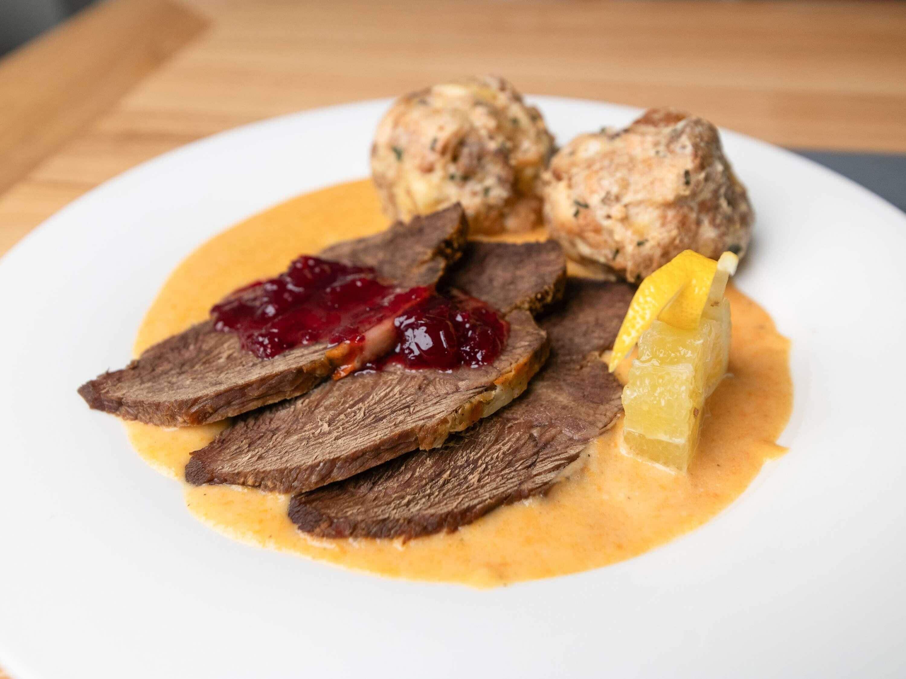 Ein Teller mit geschnittenem Fleisch, einer Kugel Soße und einem Stück Obst.