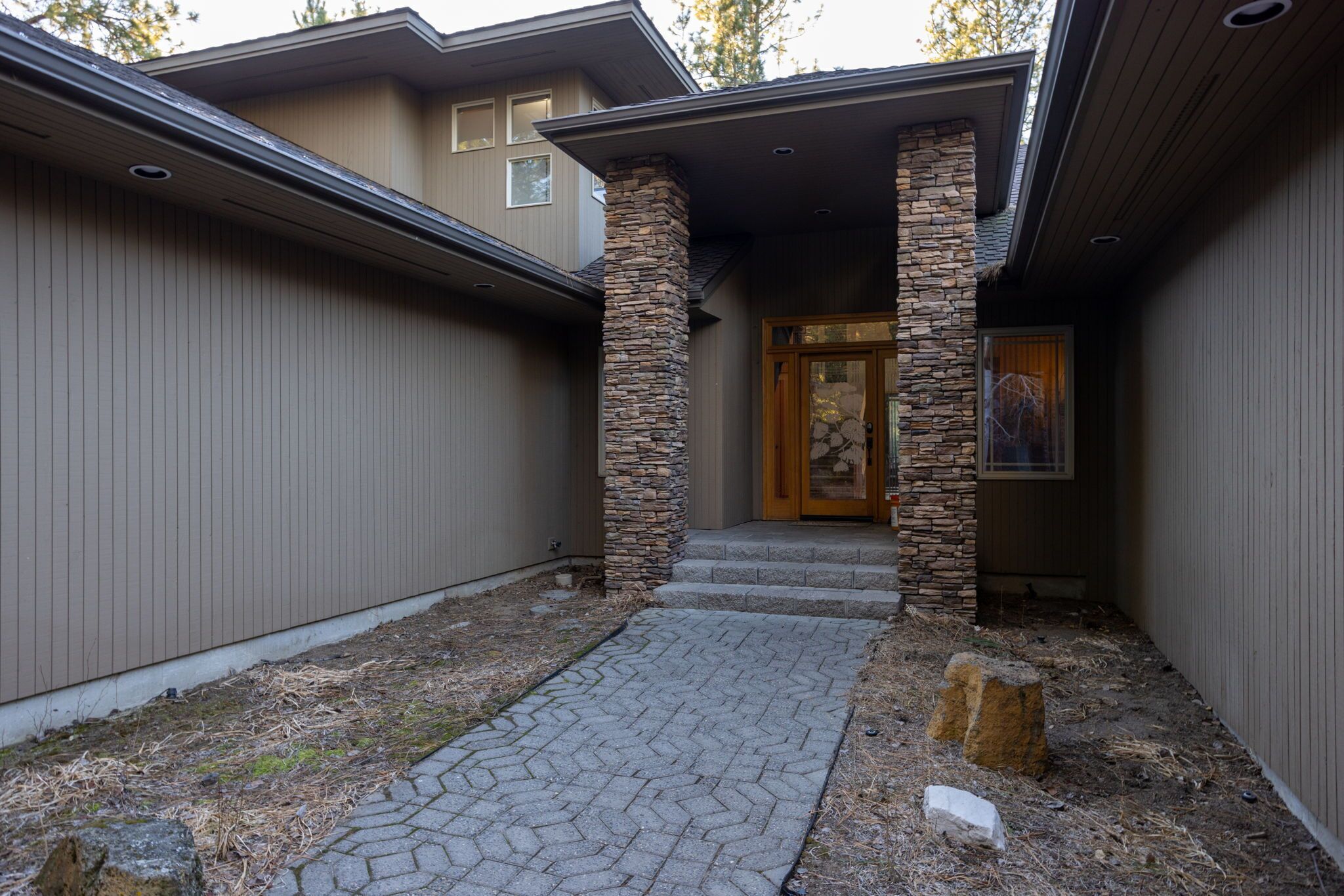 A modern house with a stone column entrance, a paved pathway, and a wooden door.
