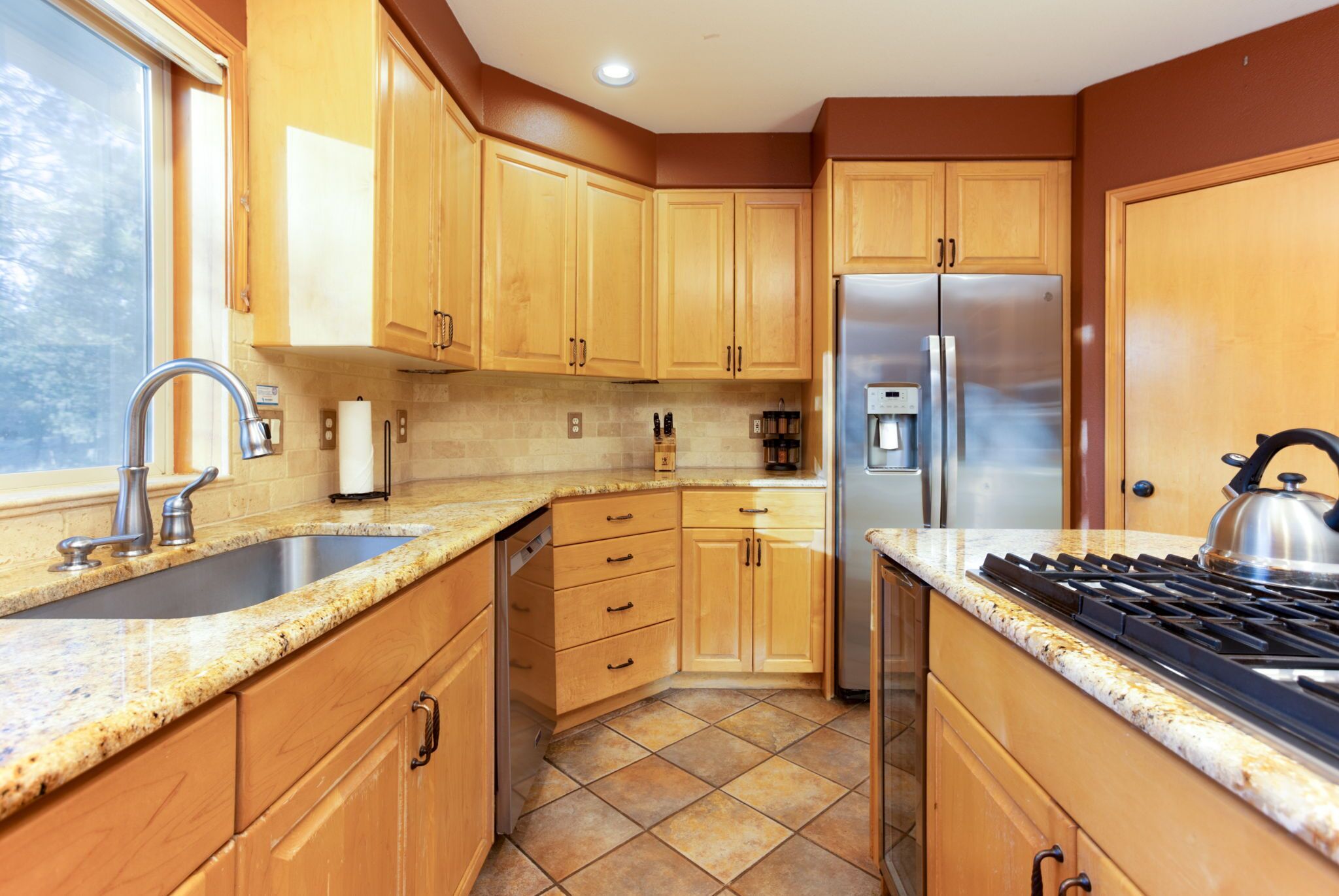 Une cuisine avec des meubles de rangement en bois, un réfrigérateur en acier inoxydable, une cuisinière à gaz et un évier.