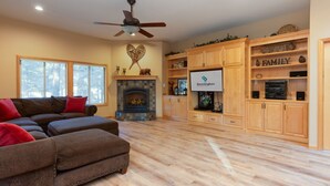 A spacious living room with a fireplace, wooden cabinets, and a television. - Cypress 4 - Huge Home, Foosball, BBQ, Dog Friendly (Sunriver)