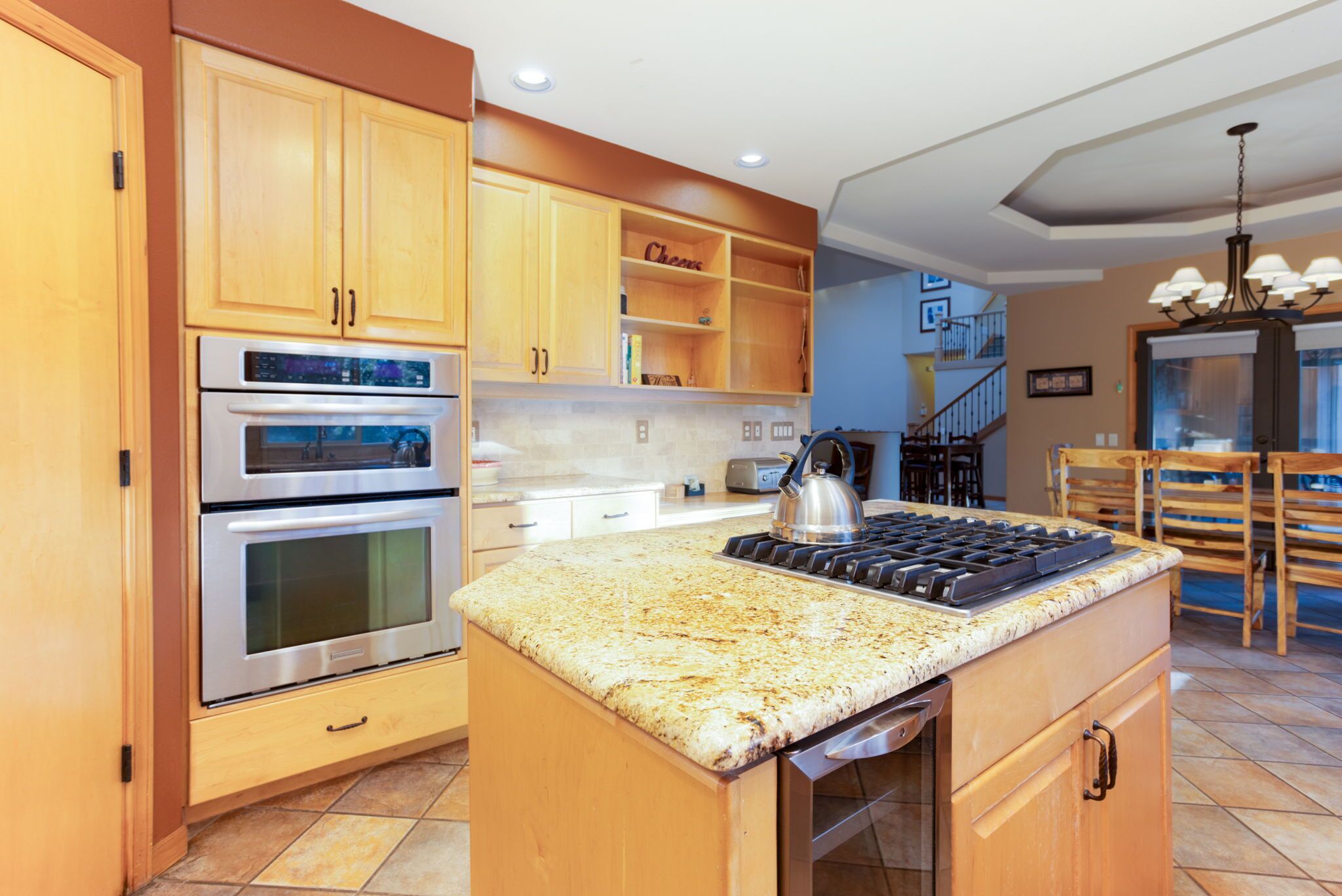 Una cocina con gabinetes de madera, electrodomésticos de acero inoxidable, encimera de granito y una escalera que sube a otro nivel.