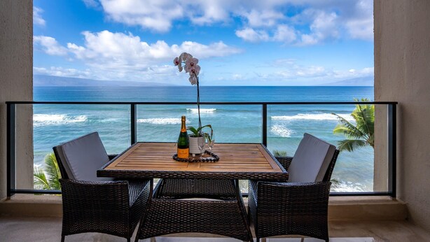 A balcony with a wooden table, wicker chairs, a bottle, a plant, and a decorative orchid.
