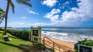 A beach entrance with a warning sign, a stone pathway, and a railing leading to the beach.