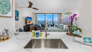 A modern kitchen with a large sink, a ceiling fan, and a view of the ocean.