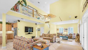 A spacious living area with a high ceiling, a balcony with a view, and a kitchen area.