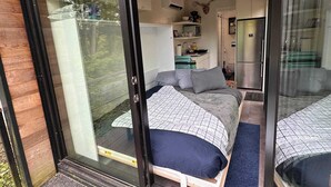 Un dormitorio moderno con una cama grande, una kitchenette pequeña y un ventanal corredero que da a un balcón.