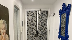 A hallway with a double door featuring floral wallpaper, a blue ornate mirror, and a small blue table. - The Comfortable House 2 (Genova)