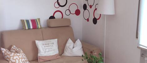 A living room with a beige sofa, a white coffee table, a potted plant, and a wall with circular patterns.