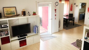 A living room with a flat-screen TV, a bookshelf, and a dining area with a table and chairs. - Sunny, cosy and quiet appartment with a view to Salzburg, close to the city (Ainring)
