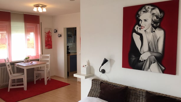 A bedroom with a bed, a red wall, a painting, a desk, and a chair. - Sunny, cosy and quiet appartment with a view to Salzburg, close to the city (Ainring)