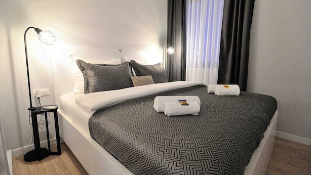 A neatly made bed with a geometric patterned bedspread, a bedside lamp, and a small table with a power outlet.