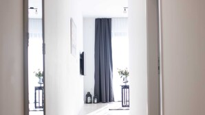 A hallway with wooden flooring, a large mirror on the left, and a door on the right.
