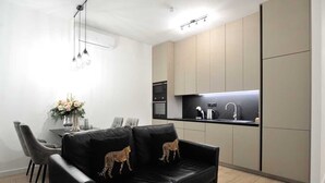 A modern kitchen with a black countertop, a built-in oven, and a sink. There is a dining area with a table and chairs, and a black leather sofa with leopard print cushions.