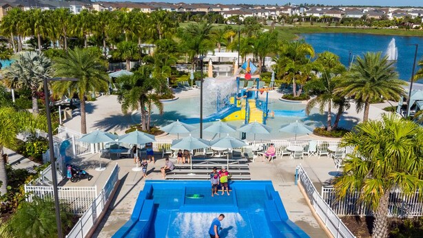 Une grande piscine extérieure avec un toboggan, entourée de palmiers et offrant une vue sur un quartier résidentiel.