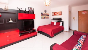 A modern hotel room with a red and black color scheme, a flat-screen TV, a bed with red bedding, a sofa with colorful cushions, and a chandelier. - Ondas Verdes - Central, Pool & Tenis Court (Albufeira)