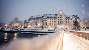 Un hotel cubierto de nieve con un río al frente, iluminado por farolas.